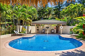 A circular pool with a tiled edge, surrounded by lounge chairs and a covered seating area with tables.