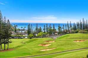 A golf course with bunkers, a water body, and a clear sky.