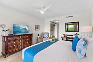 A hotel room with a bed, a dresser, a television, a ceiling fan, a window with a view, and a door leading to another room. - Kapalua 1BR Villa Near Beaches and Golf (Lahaina)