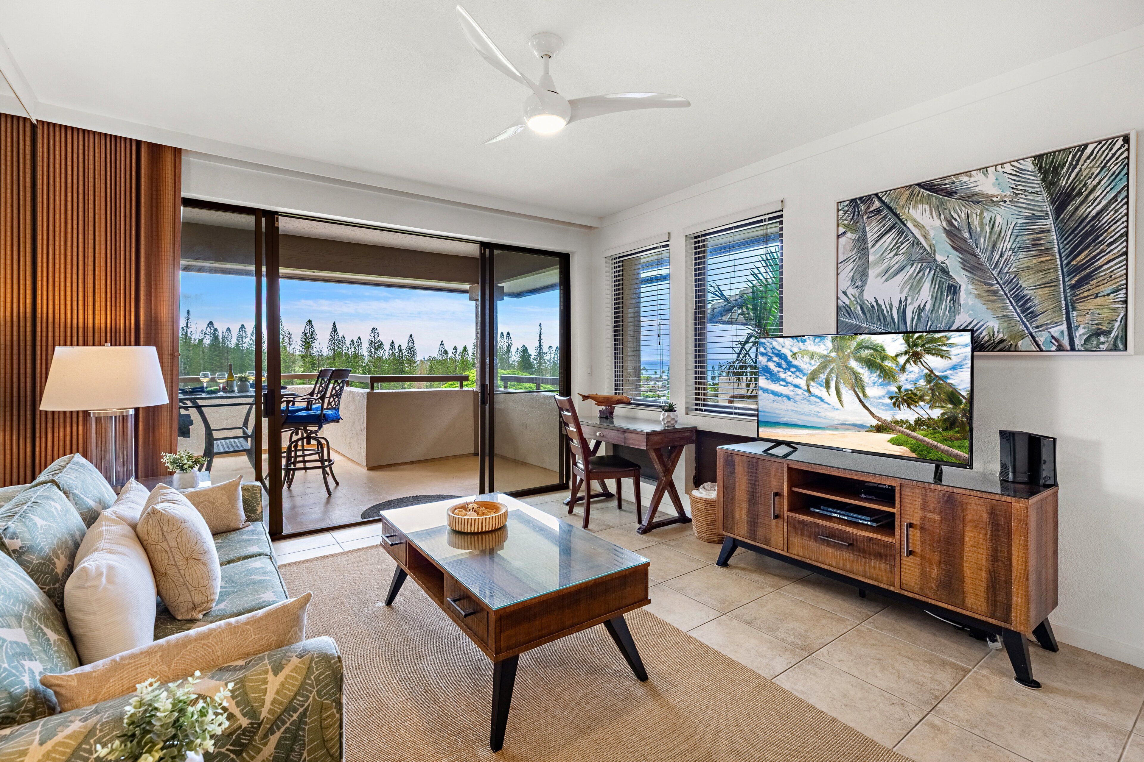 A living room with a sofa, coffee table, TV, and a balcony with a view of the beach.