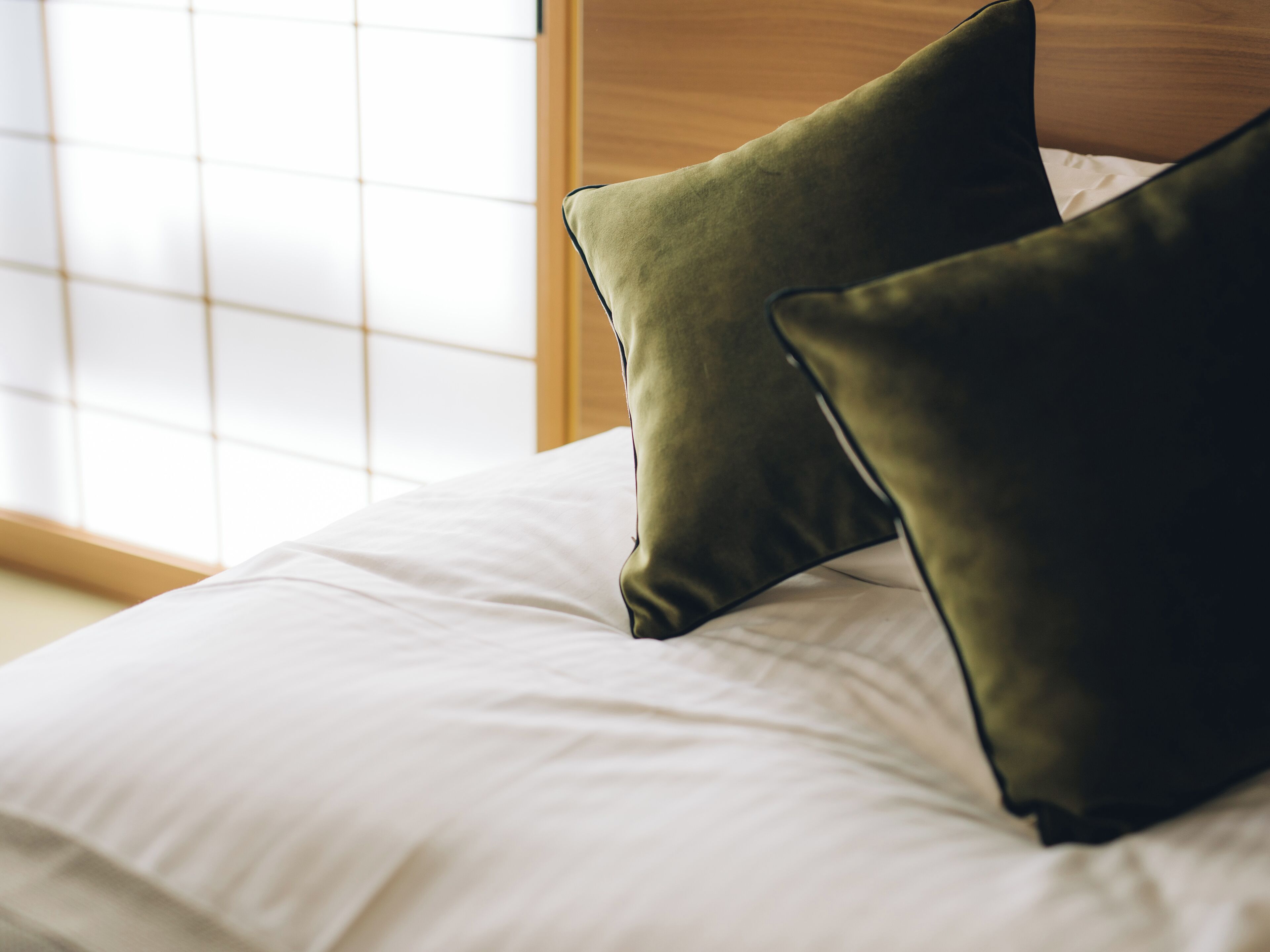 Un lit avec du linge de lit blanc et deux oreillers verts.