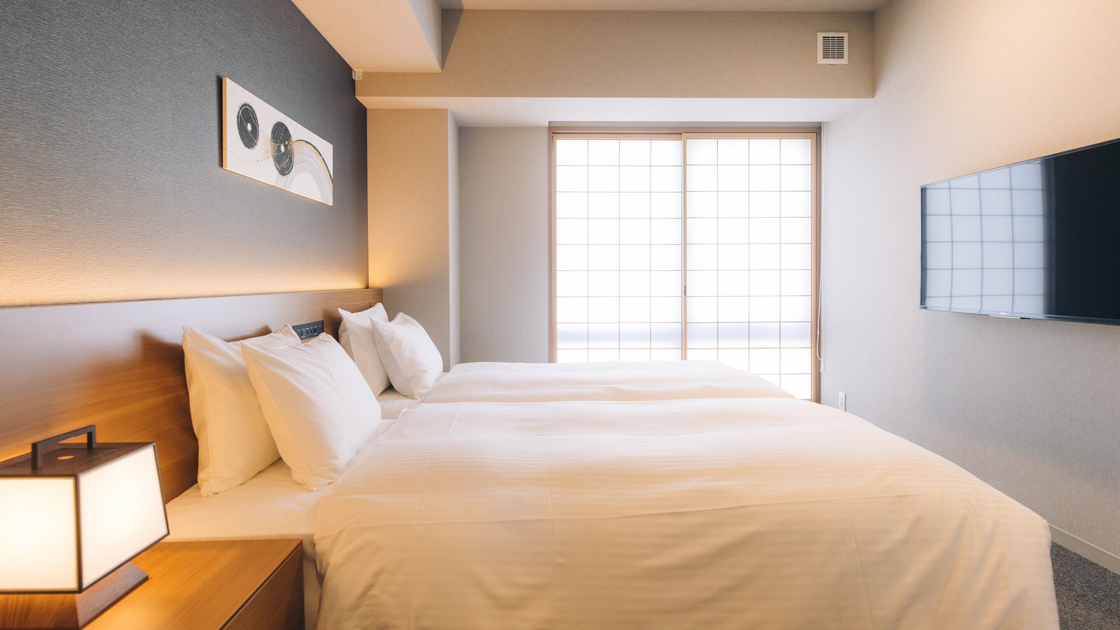 A hotel room with a bed, bedside table, wall-mounted TV, and a window with a view.