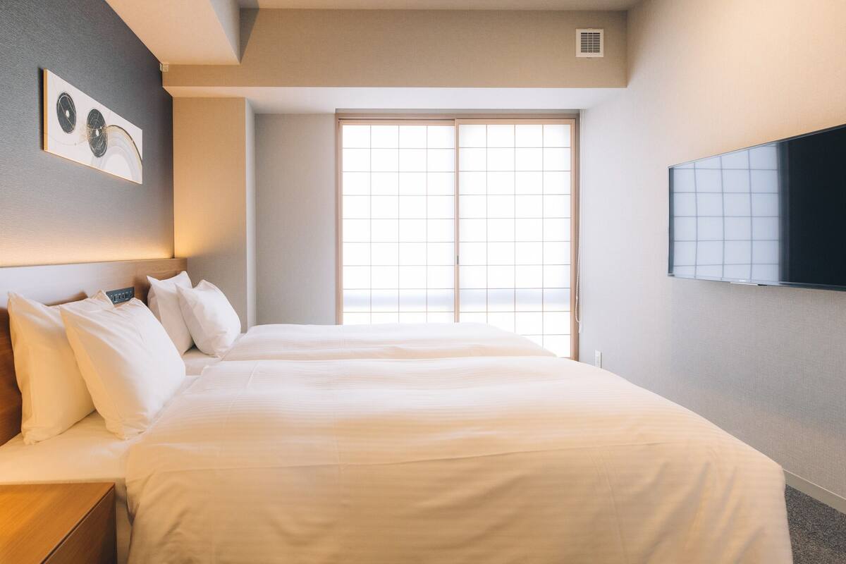 A hotel room with a bed, bedside table, wall-mounted TV, and a window with a view.
