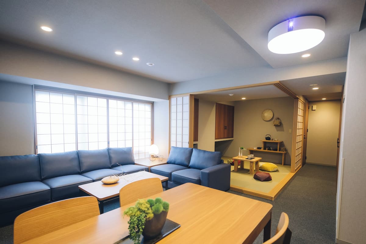 A modern living room with a sofa, a wooden dining table, and a small kitchen area.