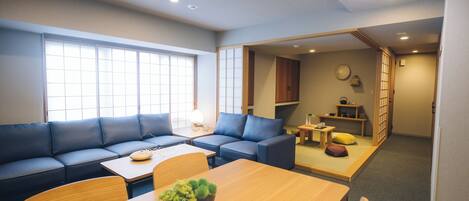 A modern living room with a sofa, a wooden dining table, and a small kitchen area.