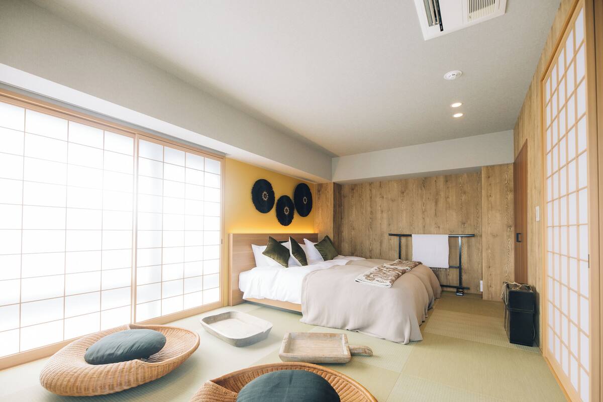 A traditional Japanese-style bedroom with tatami flooring, a low bed with a wooden headboard, and shoji screens on the windows.