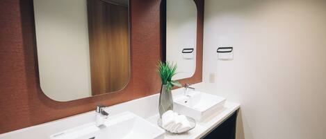 A modern bathroom with two white sinks, a mirror, and a potted plant.
