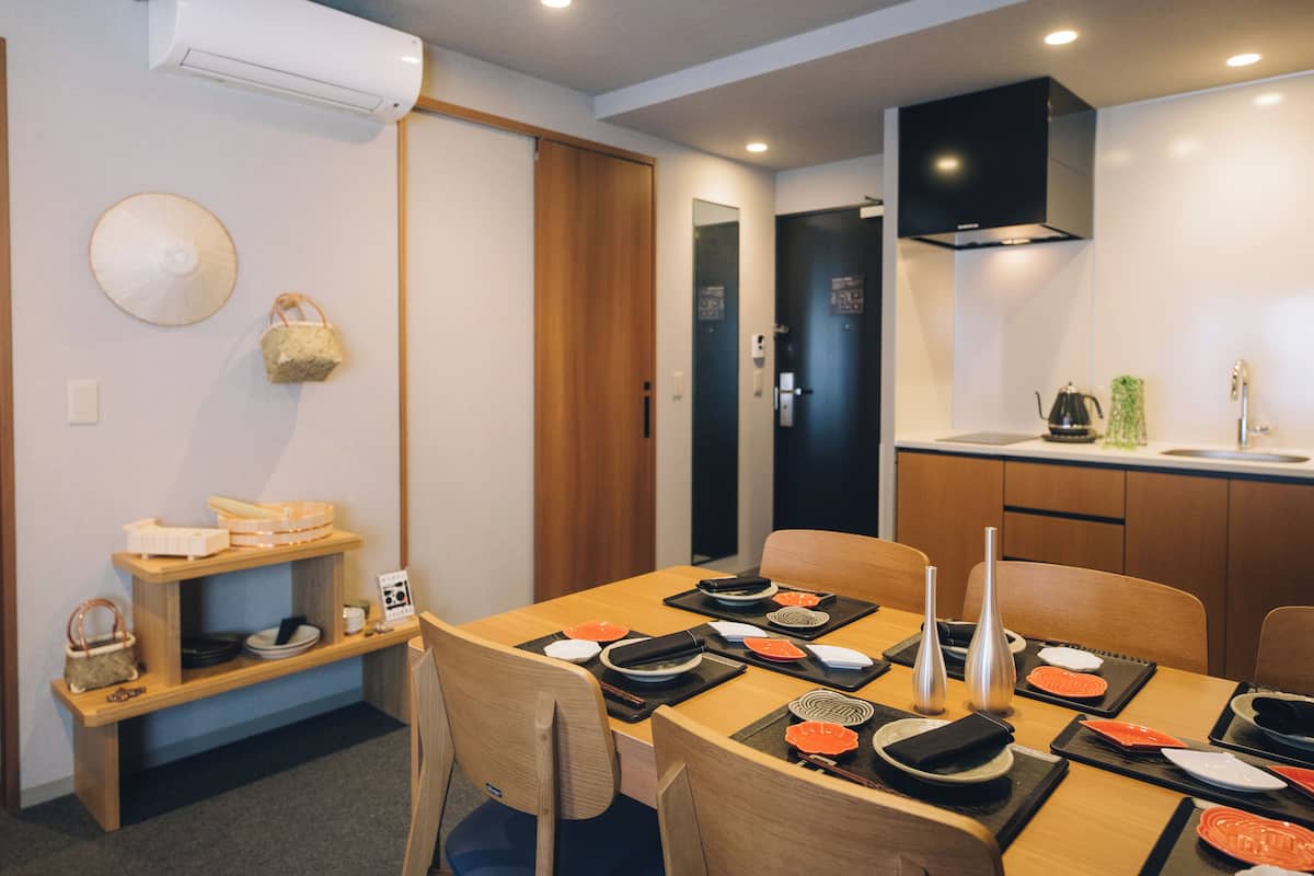A dining area with a wooden table set for two, a kitchen area with a sink and stove, and a ceiling-mounted air conditioner.