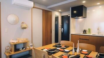 A dining area with a wooden table set for two, a kitchen area with a sink and stove, and a ceiling-mounted air conditioner.