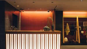 Una recepción con mostrador de madera y listones verticales, una pared roja y un perchero con prendas colgadas.