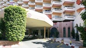 Entrada d'hotel amb zona de pàrquing coberta, una cotxe i un edifici amb balcons.