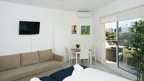 Una habitació d'hotel moderna amb un llit gran, un sofà, una taula de dinar amb cadires, una televisió penjada a la paret i un balcó amb vistes a la ciutat.