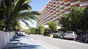 Un edifici residencial de diversos pisos amb balcons, cotxes aparcats i un carril bici blau.