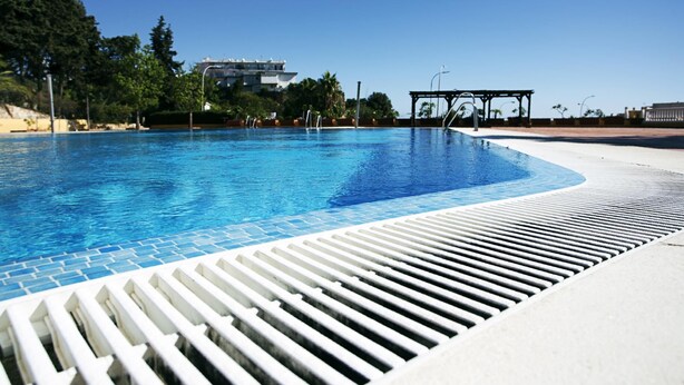 Una piscina amb superfície d'aigua blava cristal·lina, envoltada d'un solàrium de rajoles blanques.