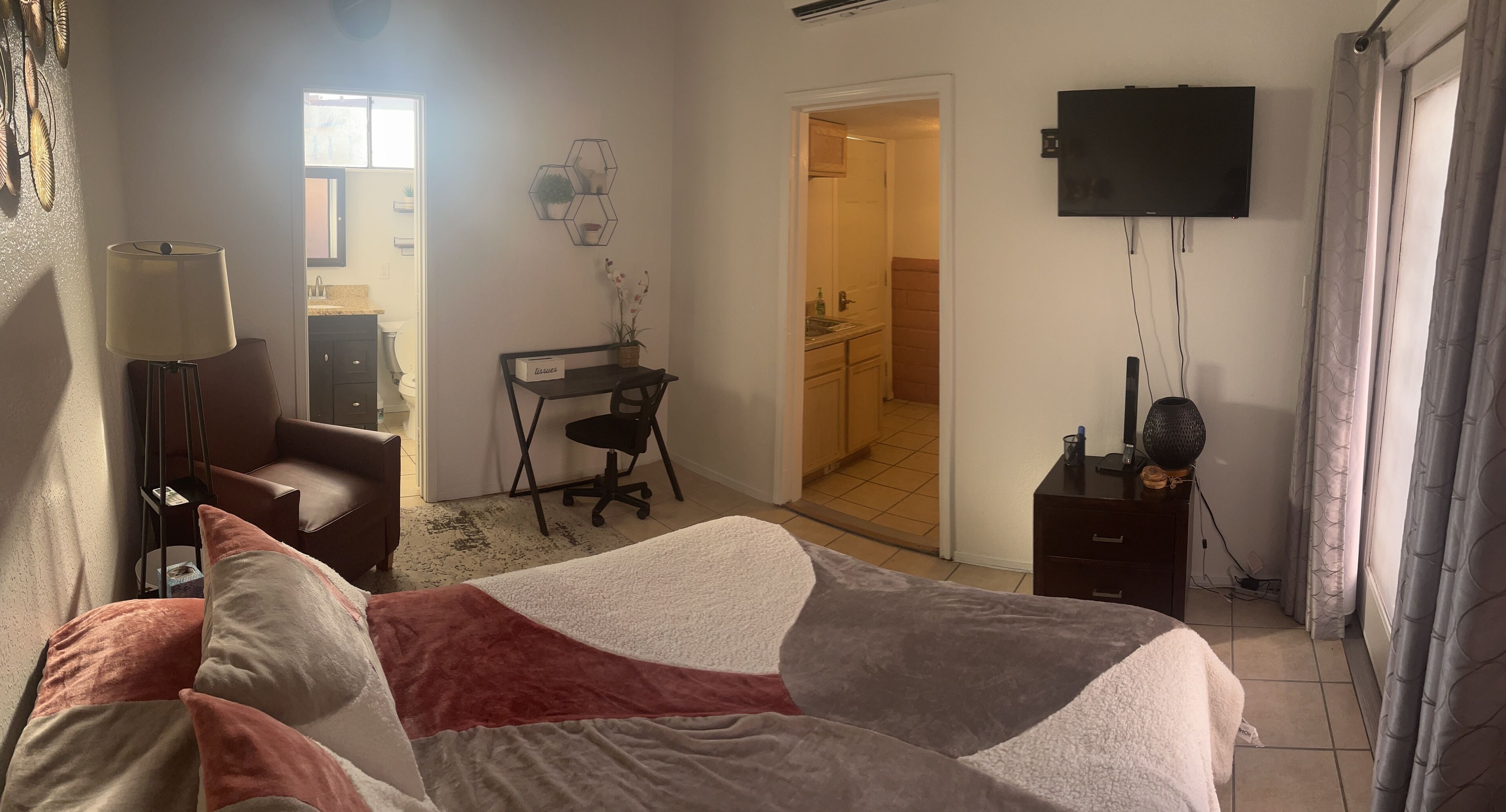 A hotel room with a bed, a desk, a chair, a TV, and a bathroom visible through an open door.
