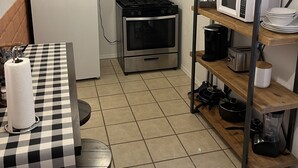Een kleine keuken met een koelkast, fornuis, oven, magnetron en een geruit tafeltje met een keukenrollenhouder.