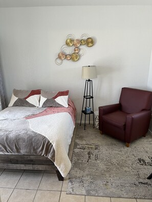A neatly arranged bedroom with a bed, a red armchair, a floor lamp, and a decorative wall piece.