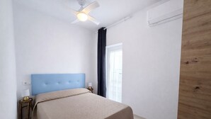 Ein Schlafzimmer mit Bett, Nachttisch, Deckenventilator und Fenster mit Vorhängen.
