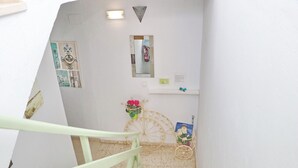 Eine Treppe mit hellgrüner Geländer führt zu einer Zwischenebene. Dort befinden sich ein kleiner Spiegel, ein Feuerlöscher und ein dekoratives Rad mit Blumen.