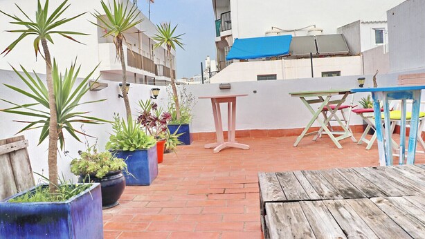 Eine Dachterrasse mit Pflanzgefäßen, einem Holztisch und Gartenmöbeln.