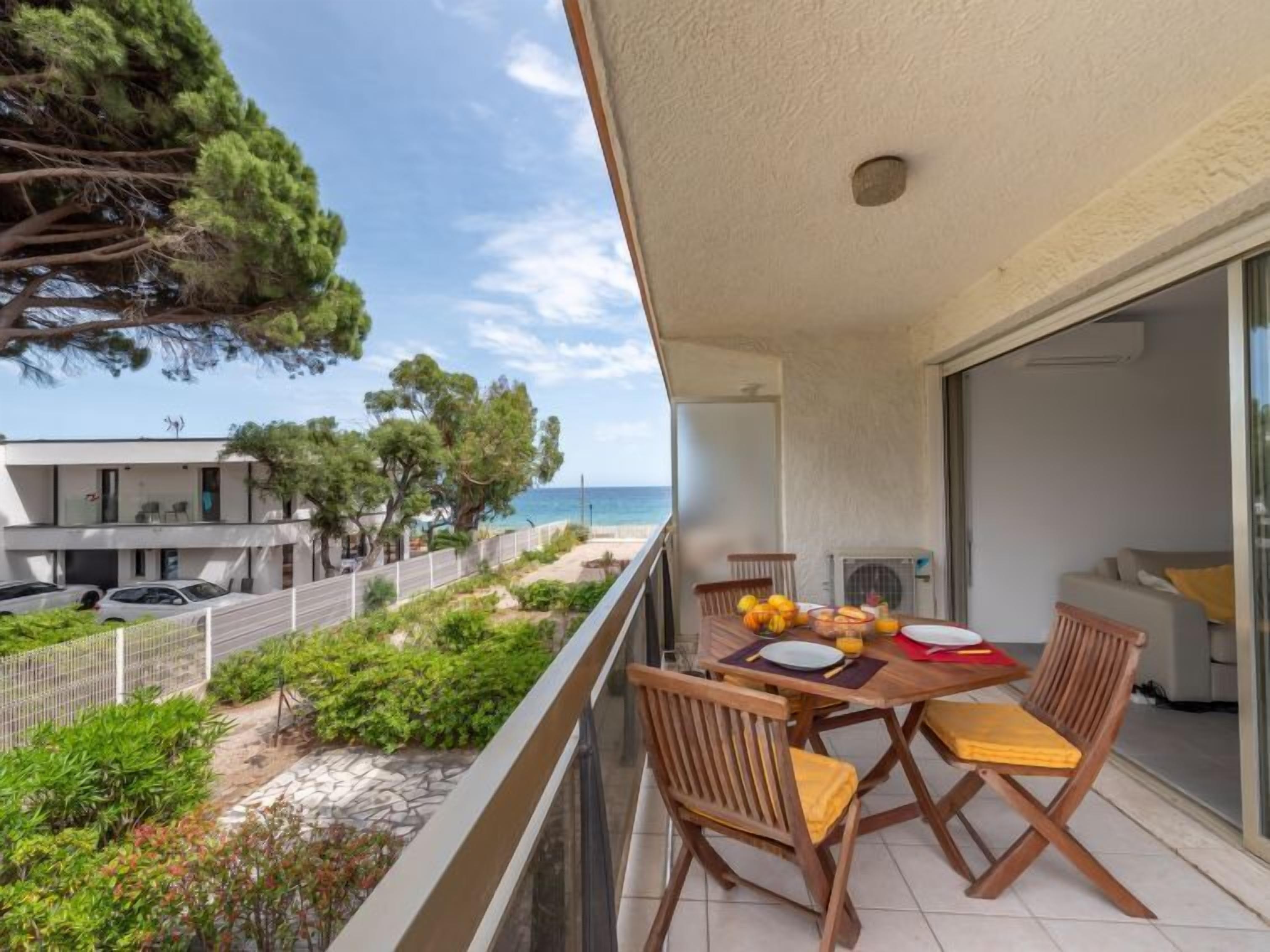Ein Balkon mit einem Tisch für zwei Personen, mit Blick auf einen Strand und ein Wohngebiet.
