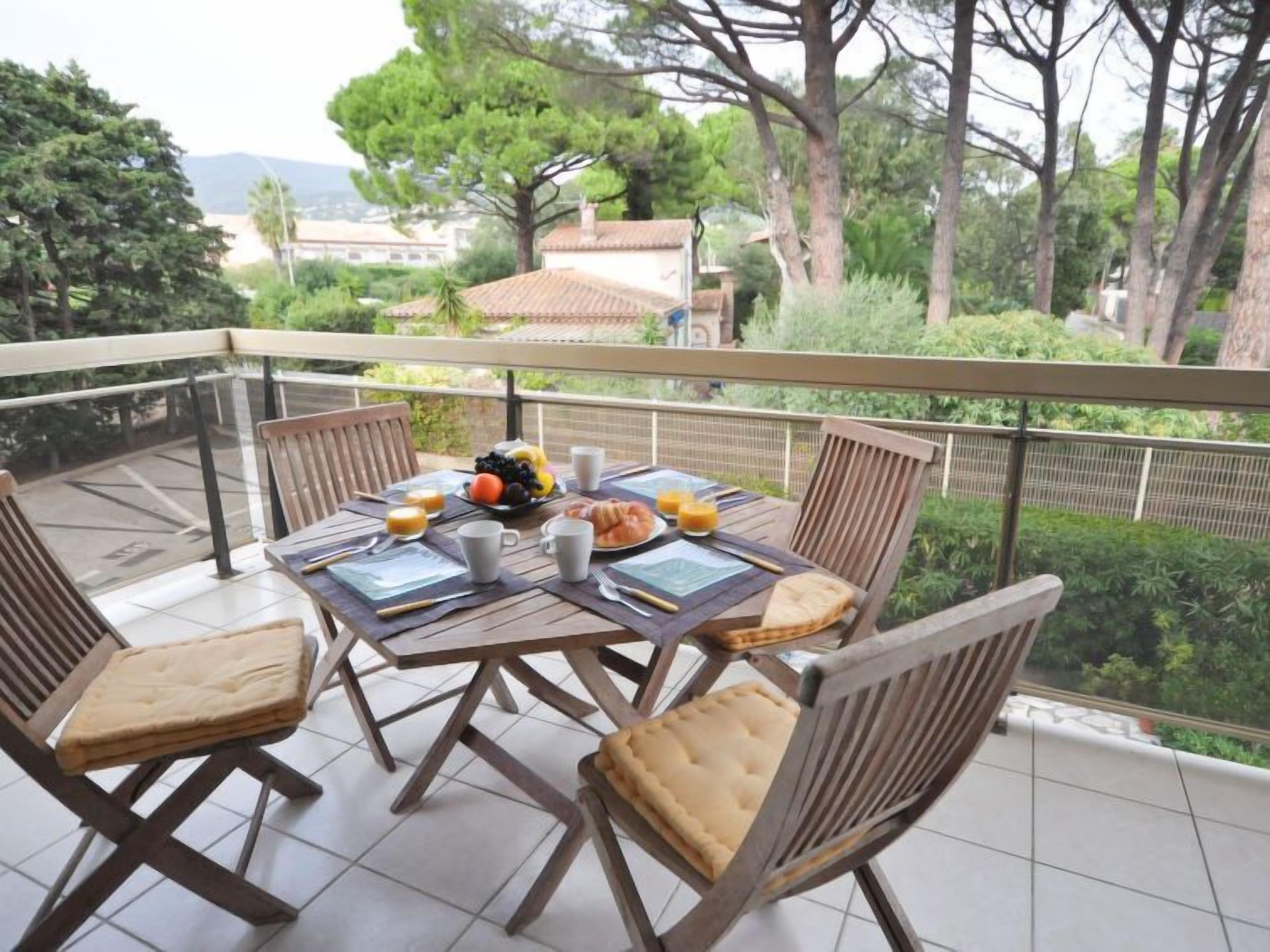 A balcony with a table set for breakfast, including fruits, croissants, and juice, surrounded by chairs.