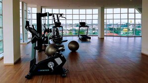 Un gimnasio amplio con máquinas de cardio, una cinta de correr y pelotas de ejercicio, con amplias ventanas que ofrecen vistas a la ciudad.