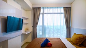 Habitación de hotel con cama, televisor montado en la pared, ventana con cortinas y vista a la ciudad.