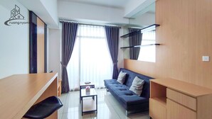 Una sala de estar moderna con un sofá, una mesa de centro y un televisor. Se ve una ventana con cortinas, una mesita y una silla.