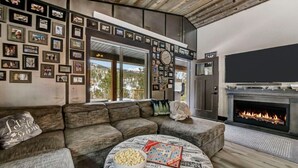 A modern living room with a sectional sofa, a fireplace, a large TV, and a wall decorated with framed photos. - Arn Barn Cabin (Lead)