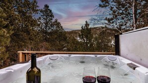 A hot tub with two glasses of red wine and a bottle of wine, surrounded by trees and a wooden deck. - Arn Barn Cabin (Lead)