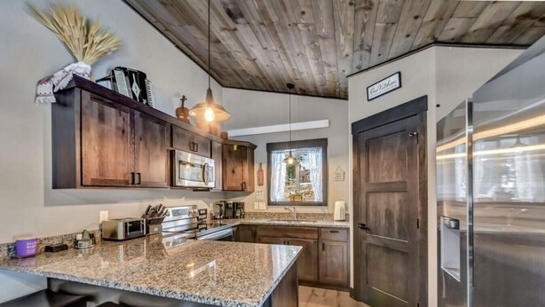 A kitchen with wooden cabinets, stainless steel appliances, a granite countertop, and a bar area. - Arn Barn Cabin (Lead)