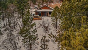 A cabin surrounded by pine trees with a wooden deck and a snow-covered landscape. - Arn Barn Cabin (Lead)