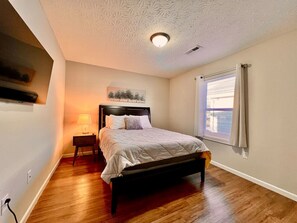 A bedroom with a bed, a nightstand, a wall-mounted TV, and a window with curtains. - 704 diamond loop new listing (Middletown)