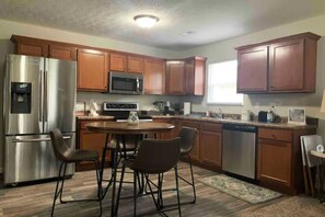 A modern kitchen with stainless steel appliances, wooden cabinets, and a dining area with chairs. - 704 diamond loop new listing (Middletown)