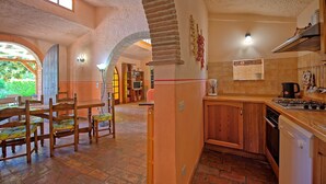 A rustic interior with a dining area, kitchen, and a view of greenery outside. - Zeffiro – Holiday country villa with  pool and tennis court near Cortona, Tuscany (Pergo)