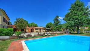 A swimming pool with lounge chairs, a brick pathway, and a building with a tiled roof in the background. - Zeffiro – Holiday country villa with  pool and tennis court near Cortona, Tuscany (Pergo)
