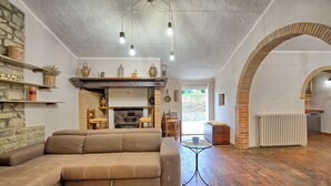 A cozy living room with a brown sofa, a fireplace, and a rustic brick floor. - Zeffiro – Holiday country villa with  pool and tennis court near Cortona, Tuscany (Pergo)