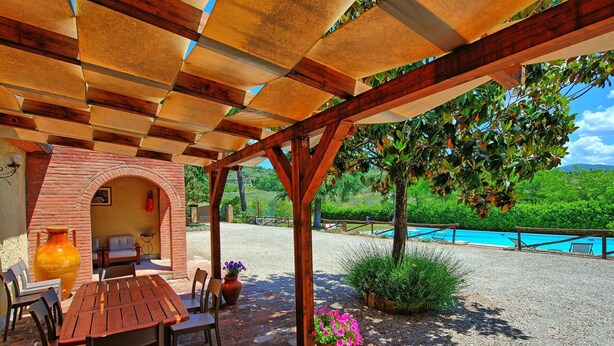 A covered outdoor seating area with a brick archway, a wooden table, and chairs. - Zeffiro – Holiday country villa with  pool and tennis court near Cortona, Tuscany (Pergo)