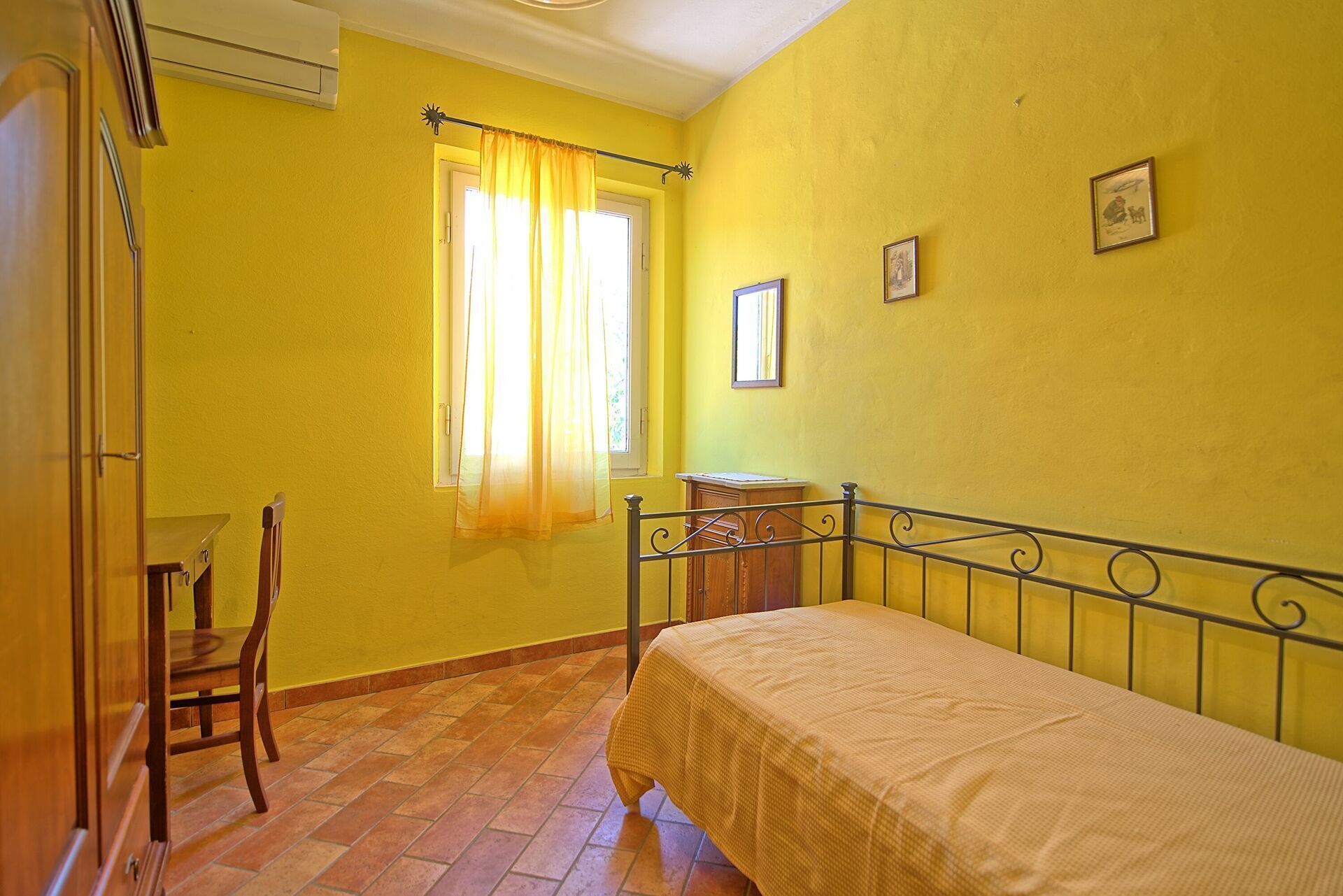 A bedroom with a bed, a chair, a small table, and a window with curtains.