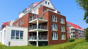 Um edifício residencial com vários andares, varandas, janelas amplas e telhado vermelho.