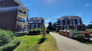 Um edifício residencial com varanda, um caminho pavimentado e um gramado bem cuidado.