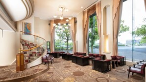 A hotel lobby with a grand staircase, seating areas, and large windows offering a view of the outdoors.