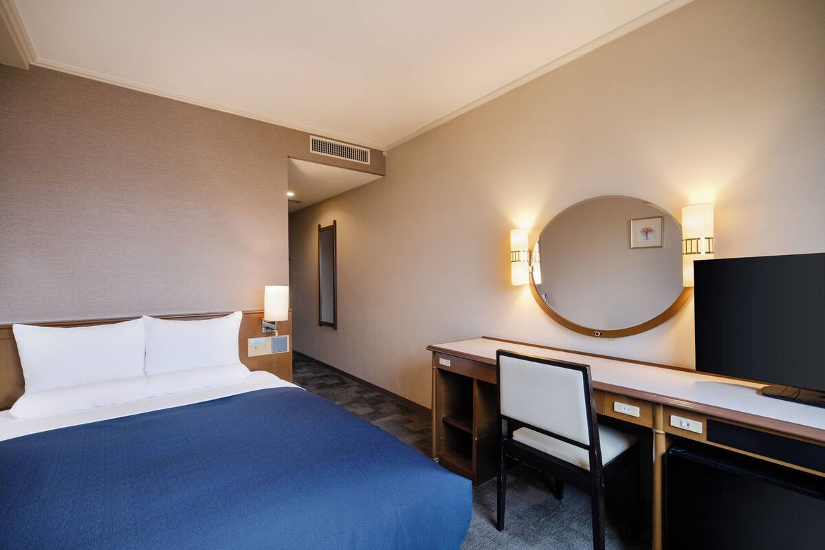 A hotel room with a bed, desk, chair, TV, and a mirror.
