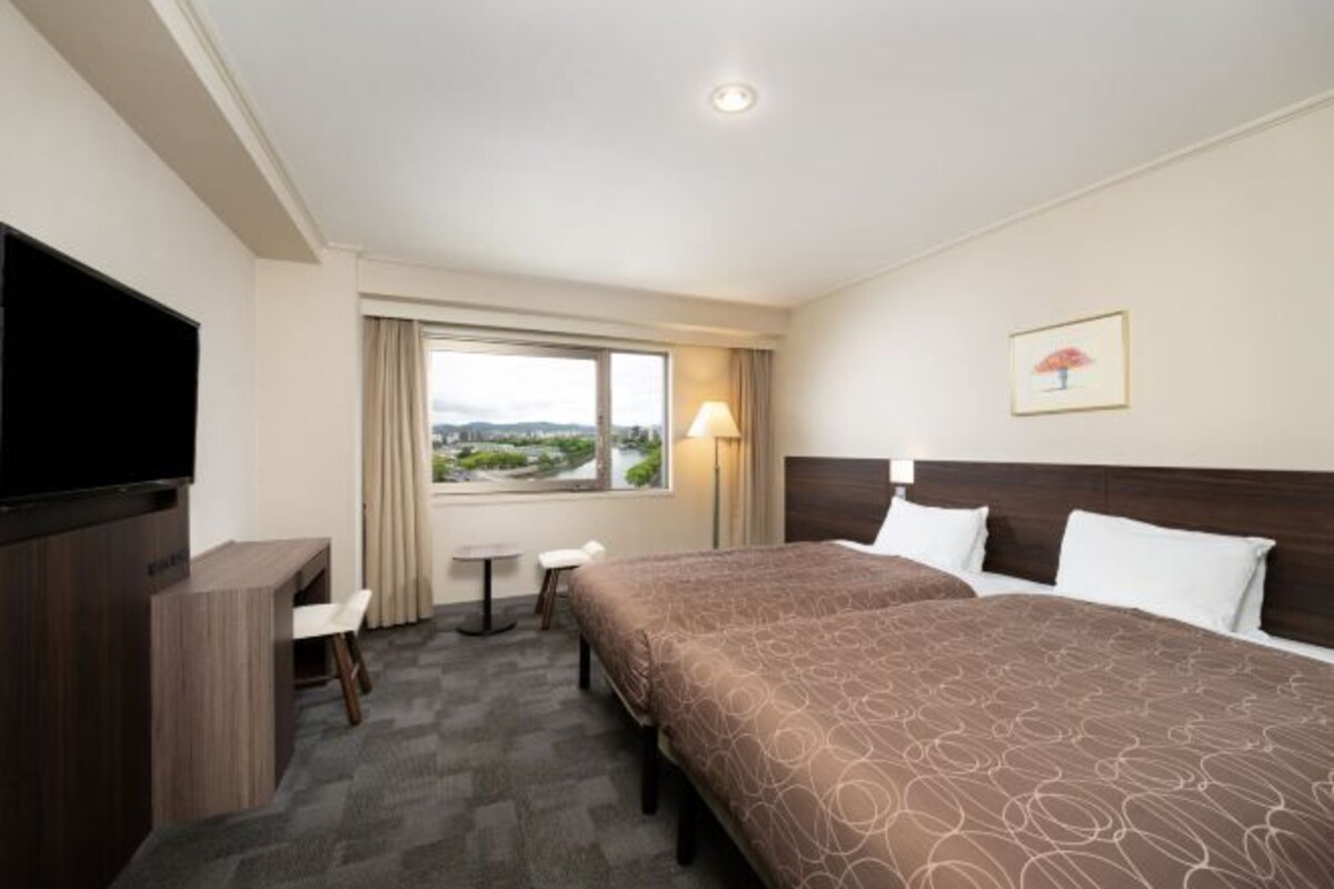 Hotelkamer met een groot bed, een televisie, een bureau, een stoel, een klein tafeltje, een lamp en een raam met uitzicht.