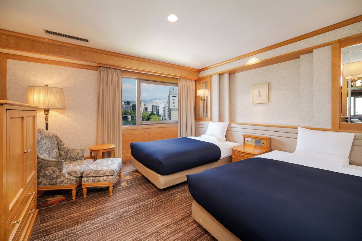 A hotel room with two beds, a sofa, a small table, and a view of the city.