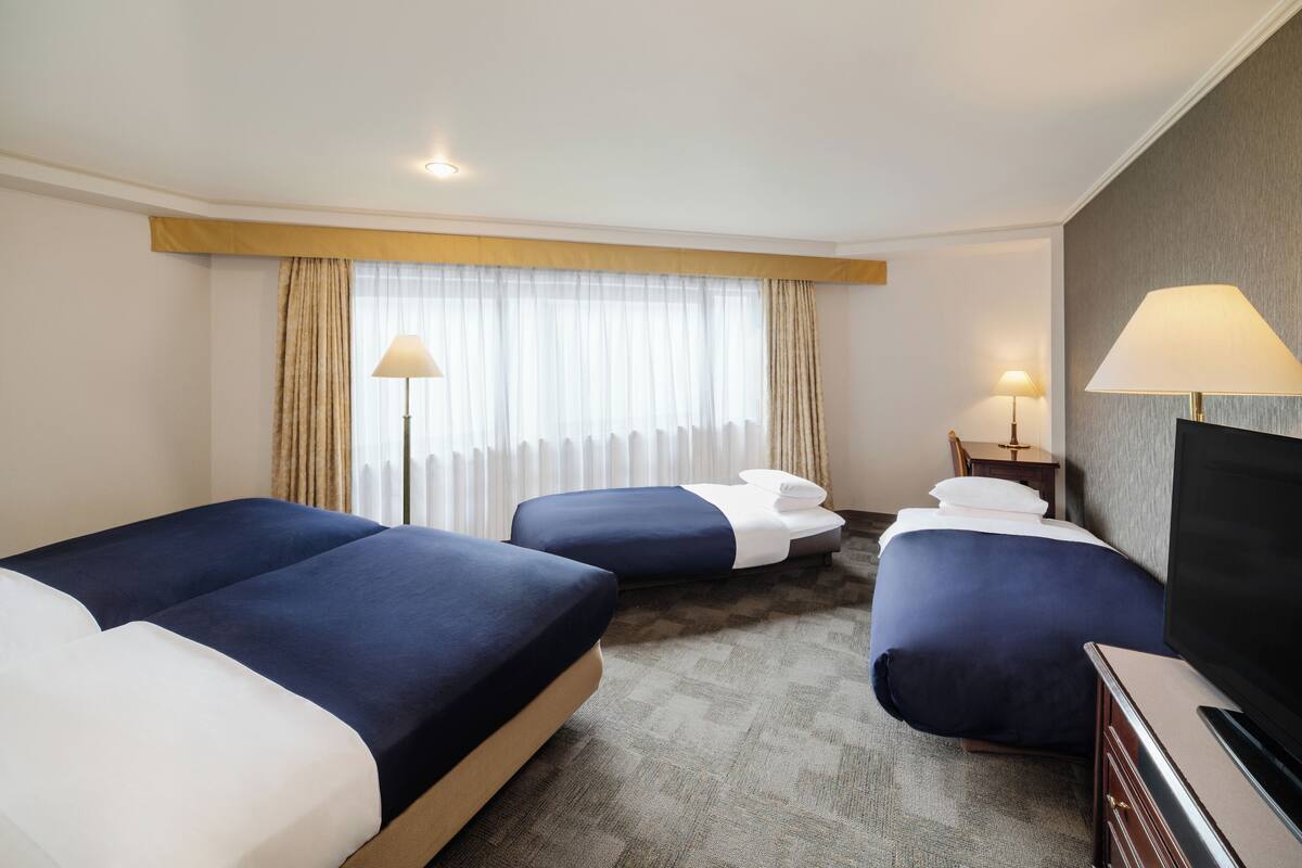 A hotel room with two beds, a television, and a desk with a lamp.