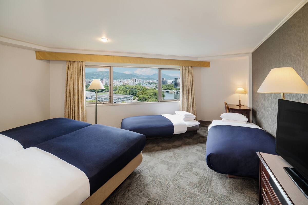 A hotel room with two beds, a TV, and a view of a cityscape.