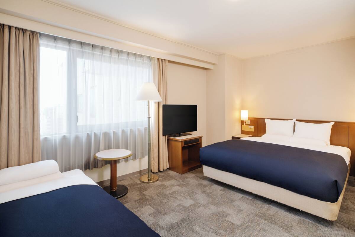 A hotel room with two beds, a television, a lamp, and a small table.