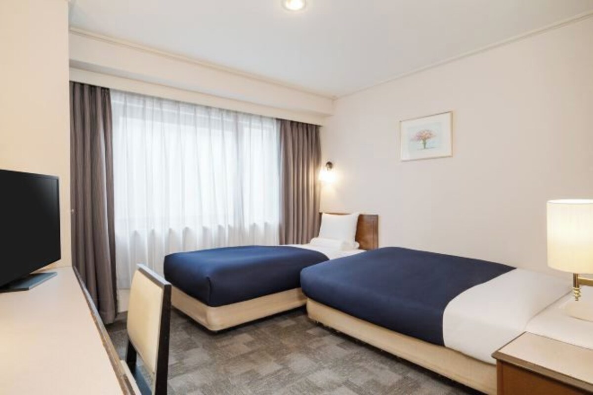 Een hotelkamer met twee bedden, een televisie, een bureau en een raam met gordijnen.